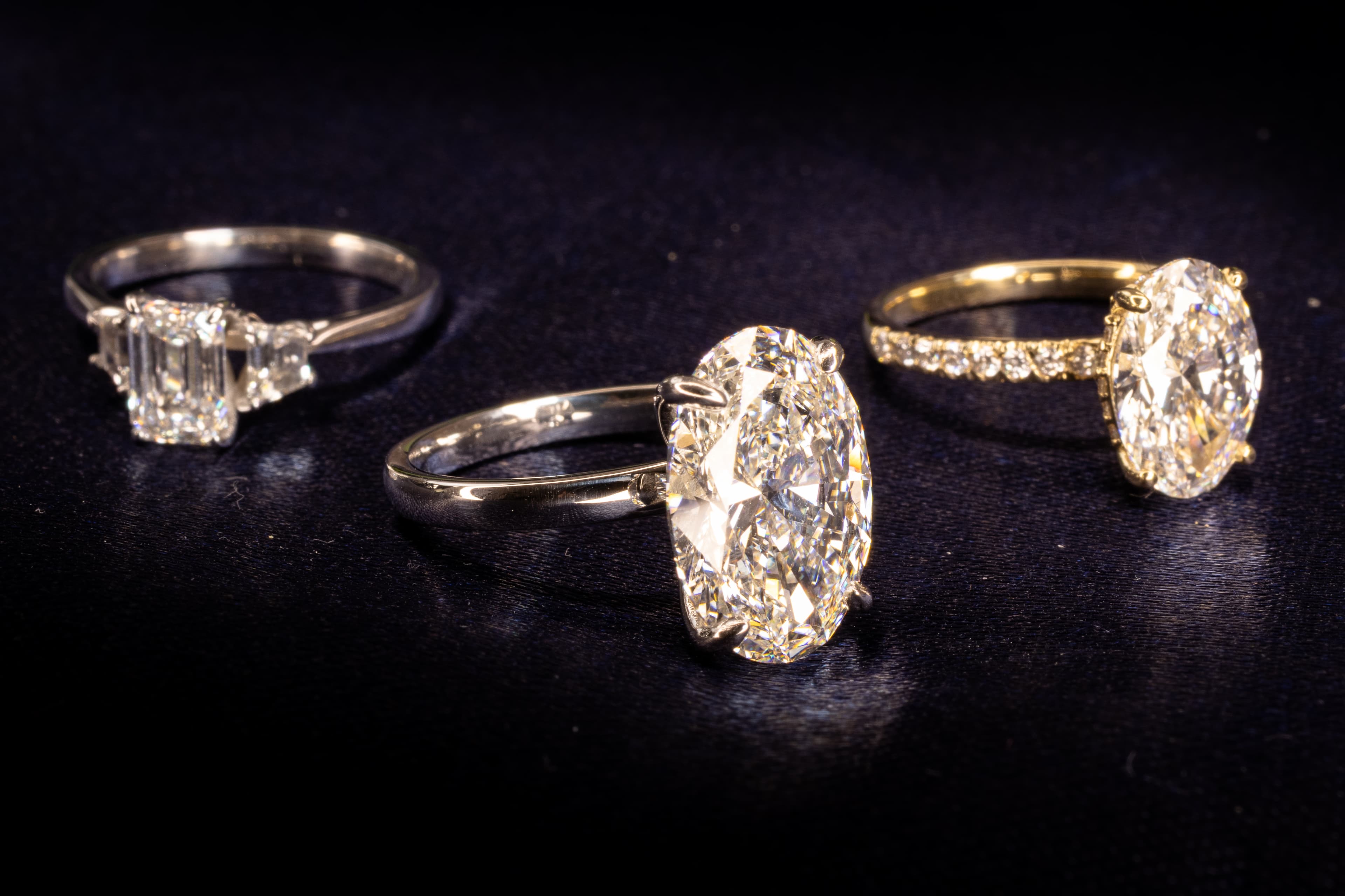 A grouping of five yellow gold engagement rings showing 2026 trends — bezel, vintage band, solitaire, hidden halo and a coloured-accent ring — on navy linen