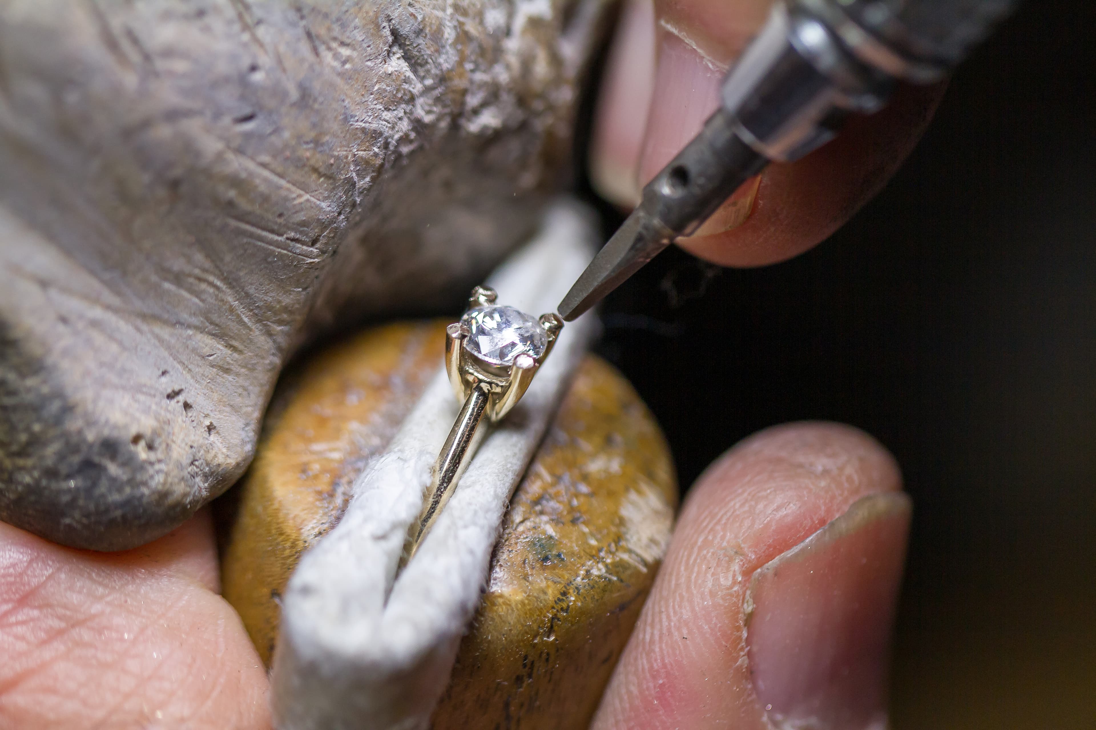A jeweller's bench flat-lay with CAD render sheets, a wax ring model, fine tools and a finished yellow gold ring