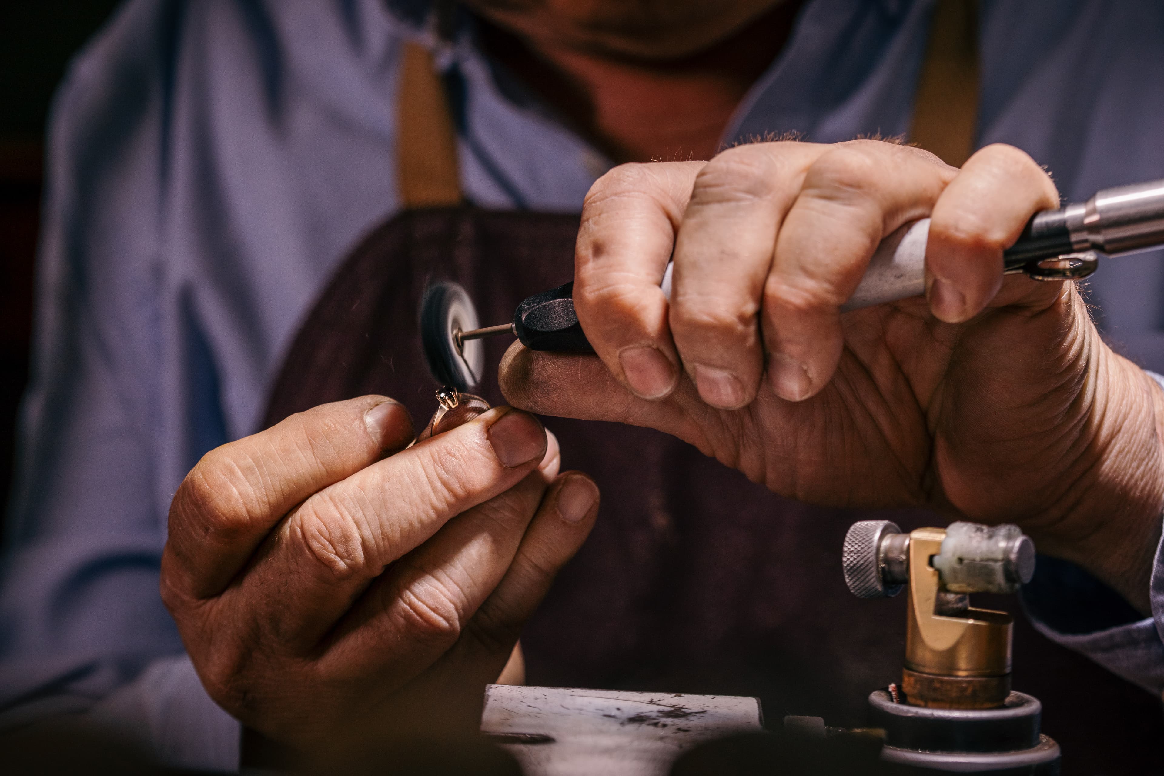A jeweller's hands setting a small diamond into a yellow gold ring at the workbench