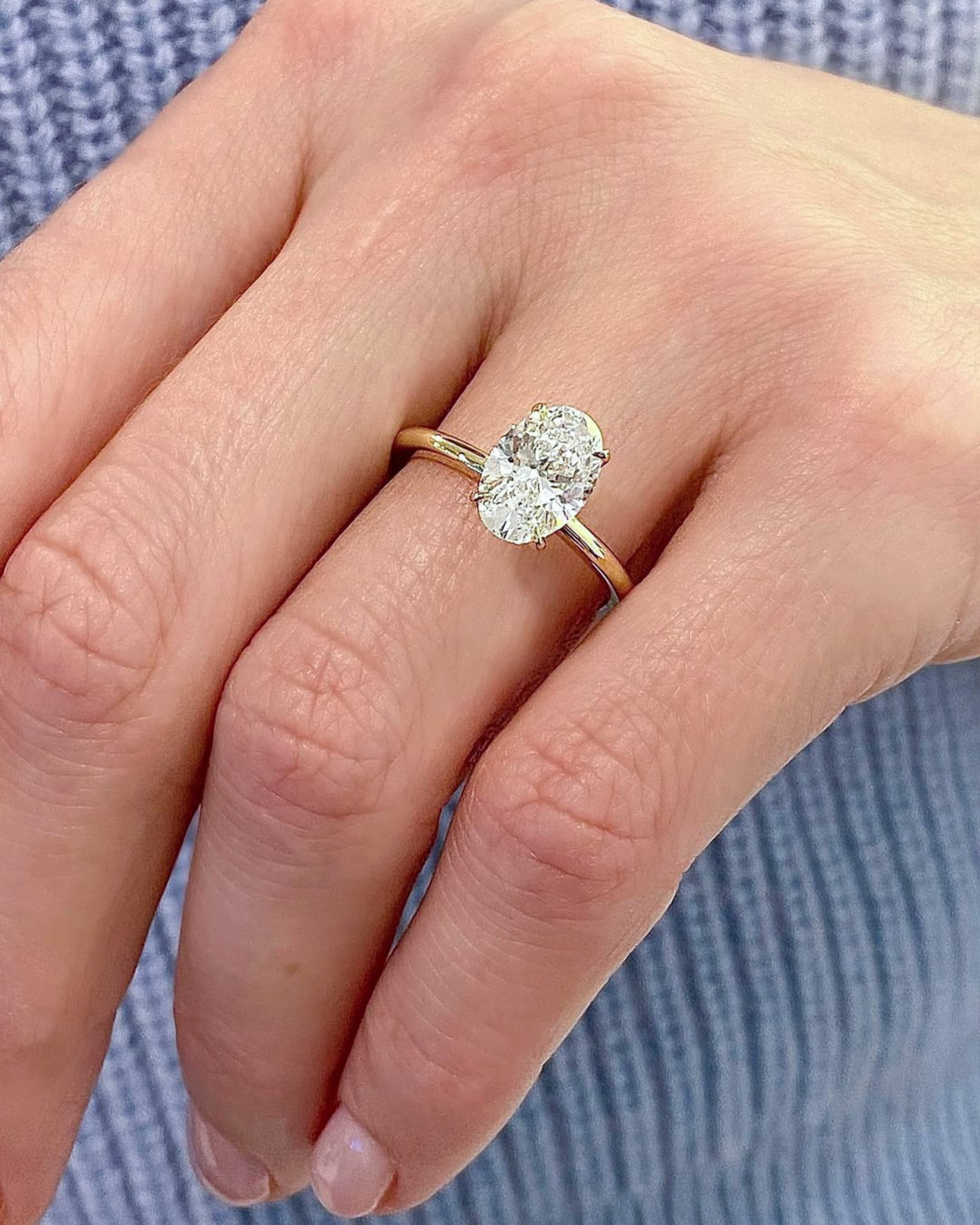 An elongated oval-cut diamond solitaire in a rose gold band, worn on a hand