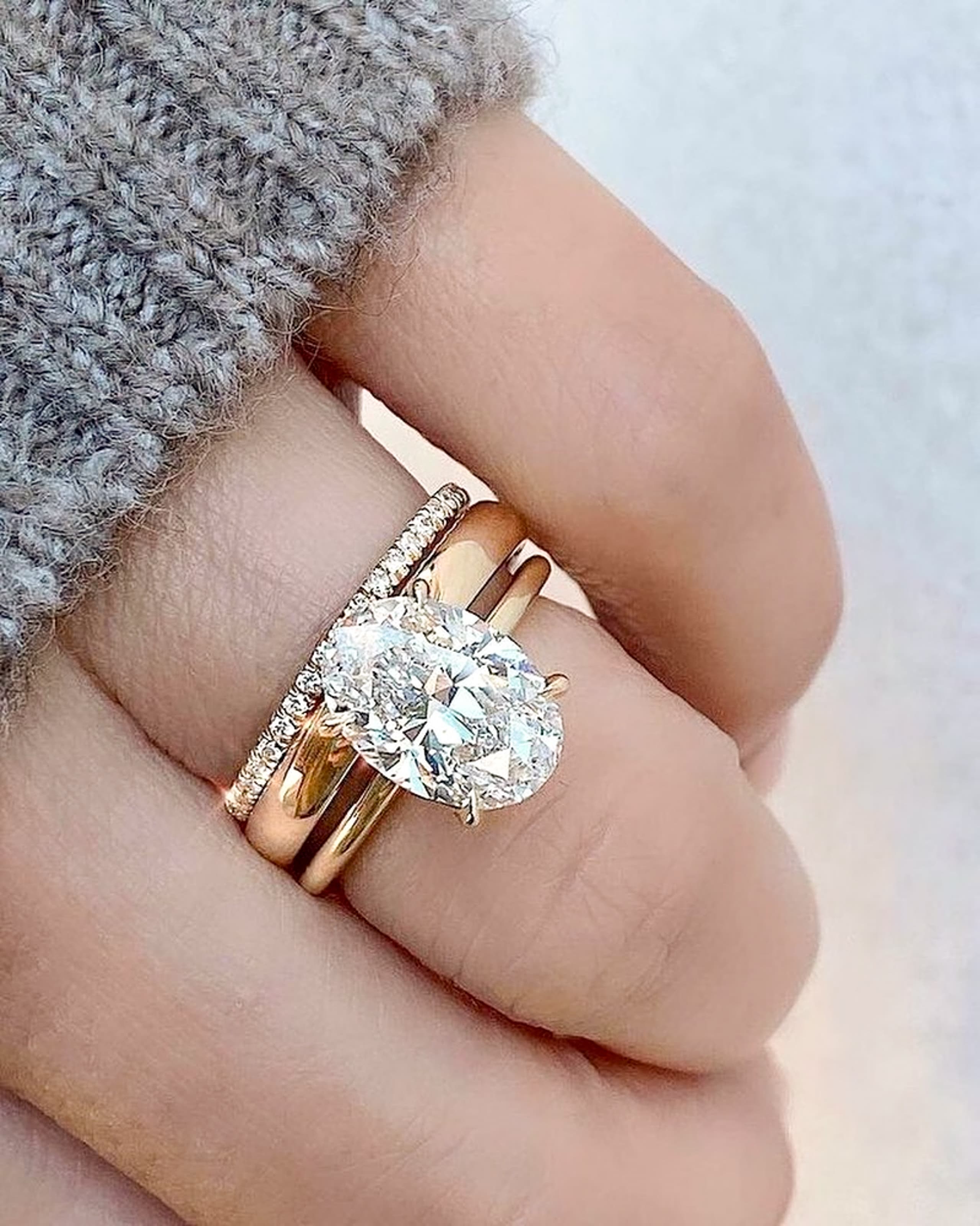 A hand at rest wearing a large oval lab-grown diamond solitaire in yellow gold