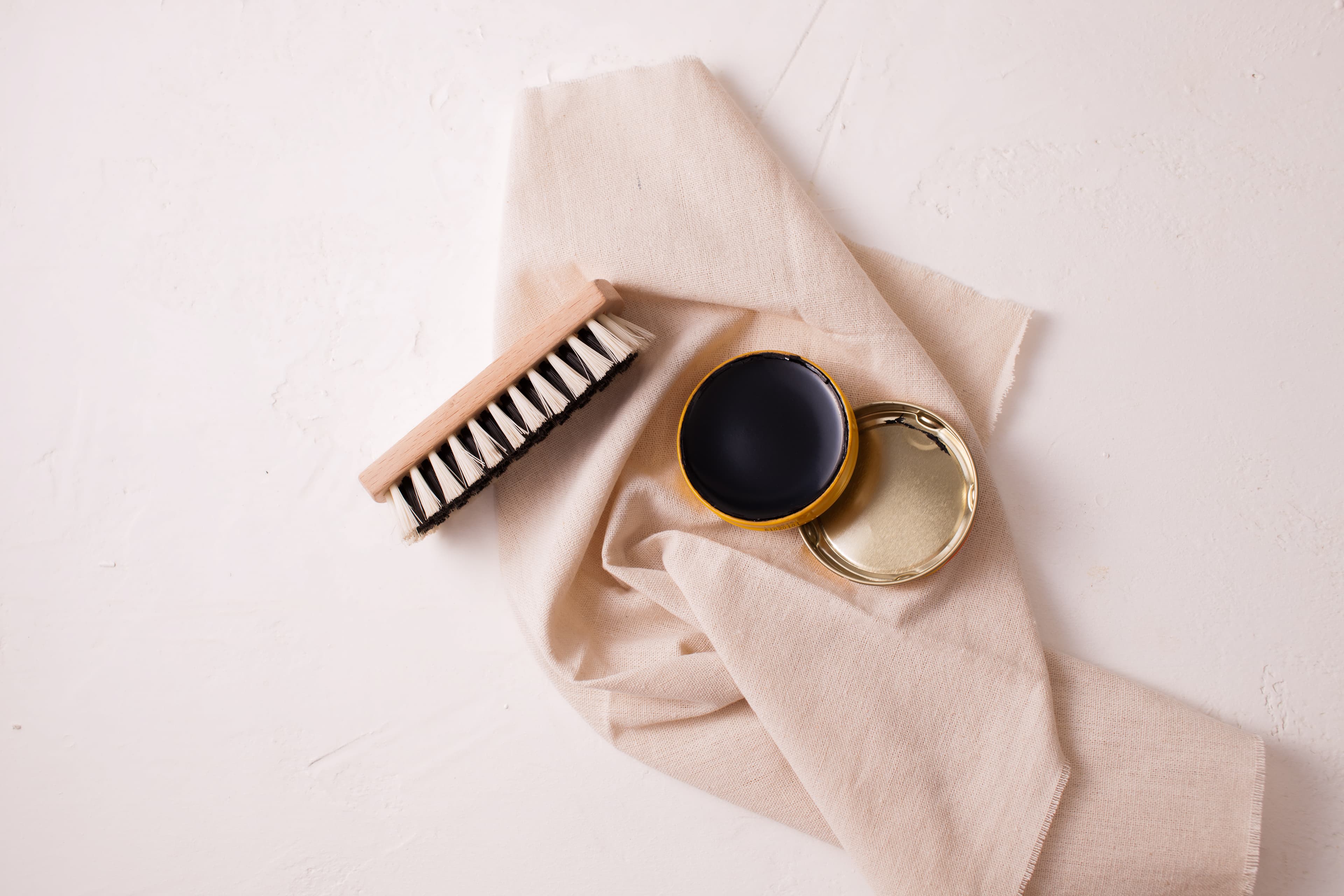 A soft natural-bristle brush resting against a yellow gold diamond ring on a lint-free cloth