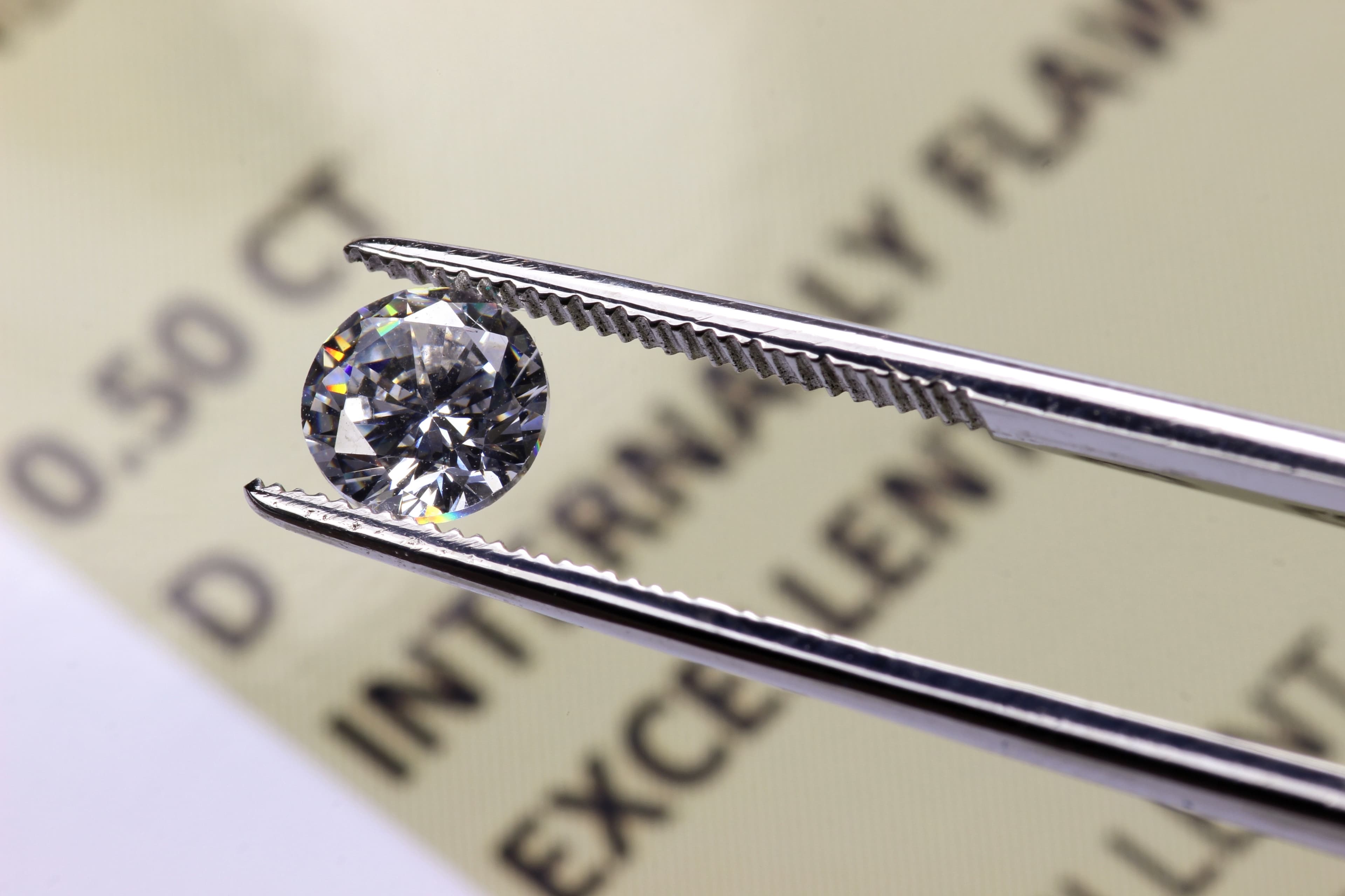 A jeweller wearing a loupe visor examining a loose lab-grown diamond held in tweezers at a workbench
